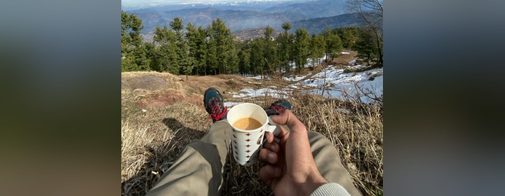 Mufeez with a cup of tea, looking out over a valley in northern Pakistan